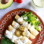 Plate with 4 flautas on top of a bed of lettuce and smothered with jalapeño sour cream