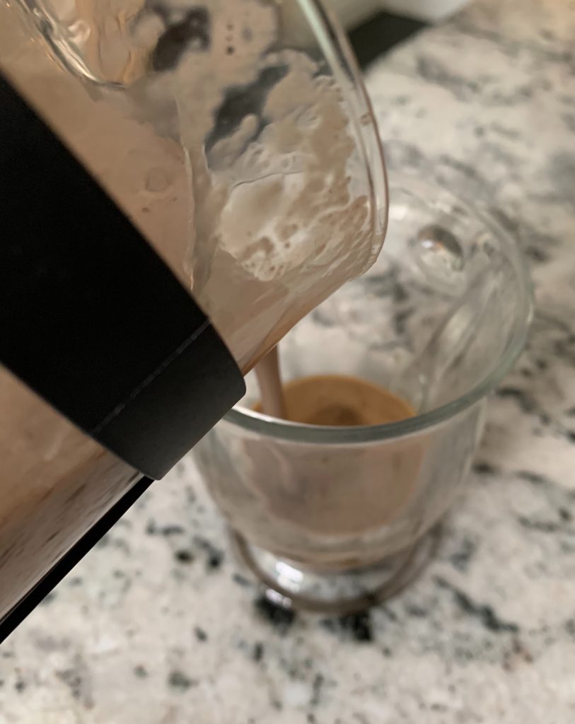 Pouring frothy chocolate milk in a mug from a French press