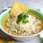 Bowl of white chicken chili with hominy with garnishes and tortillas chips