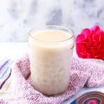 Jar of coconut condensed milk with a pink flower behind it and a colorful wooden spoon in front of it.