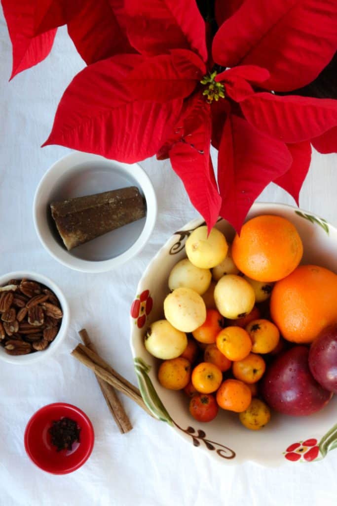Piloncillo, pecans, cloves, cinnamon sticks and a bowl of oranges, apples, tejocotes, and guavas