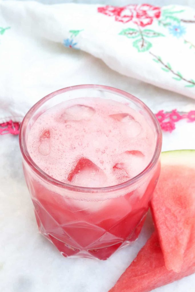Clear glass with Agua De Sandia with a piece of watermelon on the side