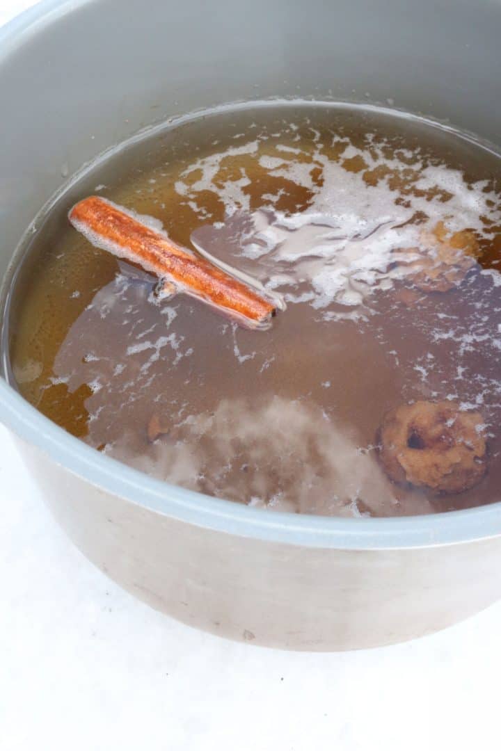 Cinnamon sticks, cloves and piloncillo simmering in water in a small pot.
