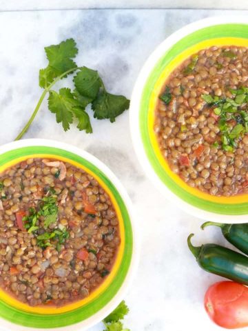 Two bowls of Mexican Lentil Soup with cilantro, jalapeños and tomatoes around them
