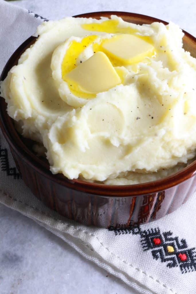 Heaping bowl of garlic mashed potatoes with two pats of butter on top