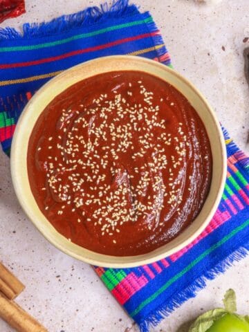 Mole Poblano in a bowl garnished with sesame seeds surrounded by ingredients