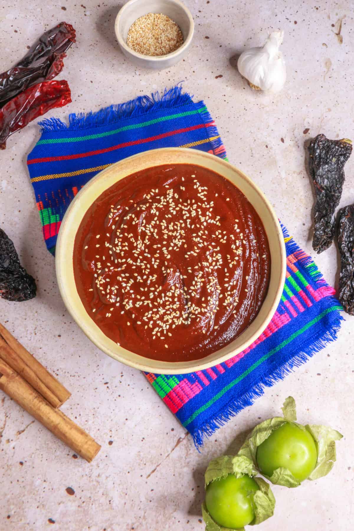 Mole Poblano in a bowl garnished with sesame seeds surrounded by ingredients