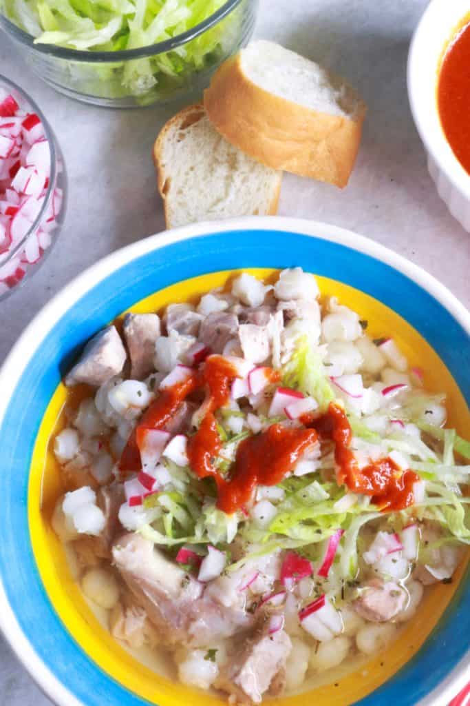 Pozole Blanco with red sauce, bowl of lettuce, sliced bread, radishes and red sauce