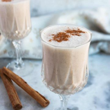 Two small wine glasses with coquito with cinnamon sticks on the table