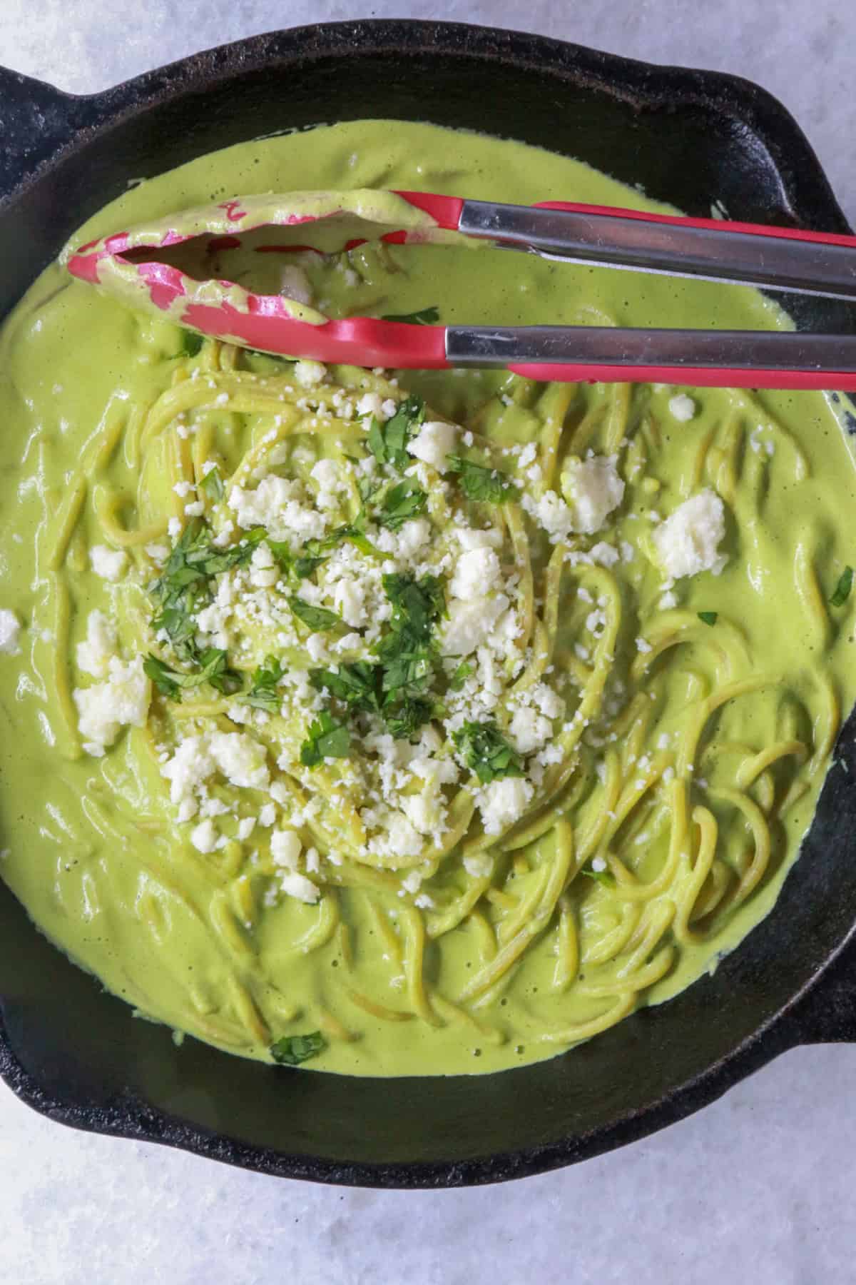 Espagueti Verde (Mexican Green Spaghetti) in a cast-iron skillet with red tongs