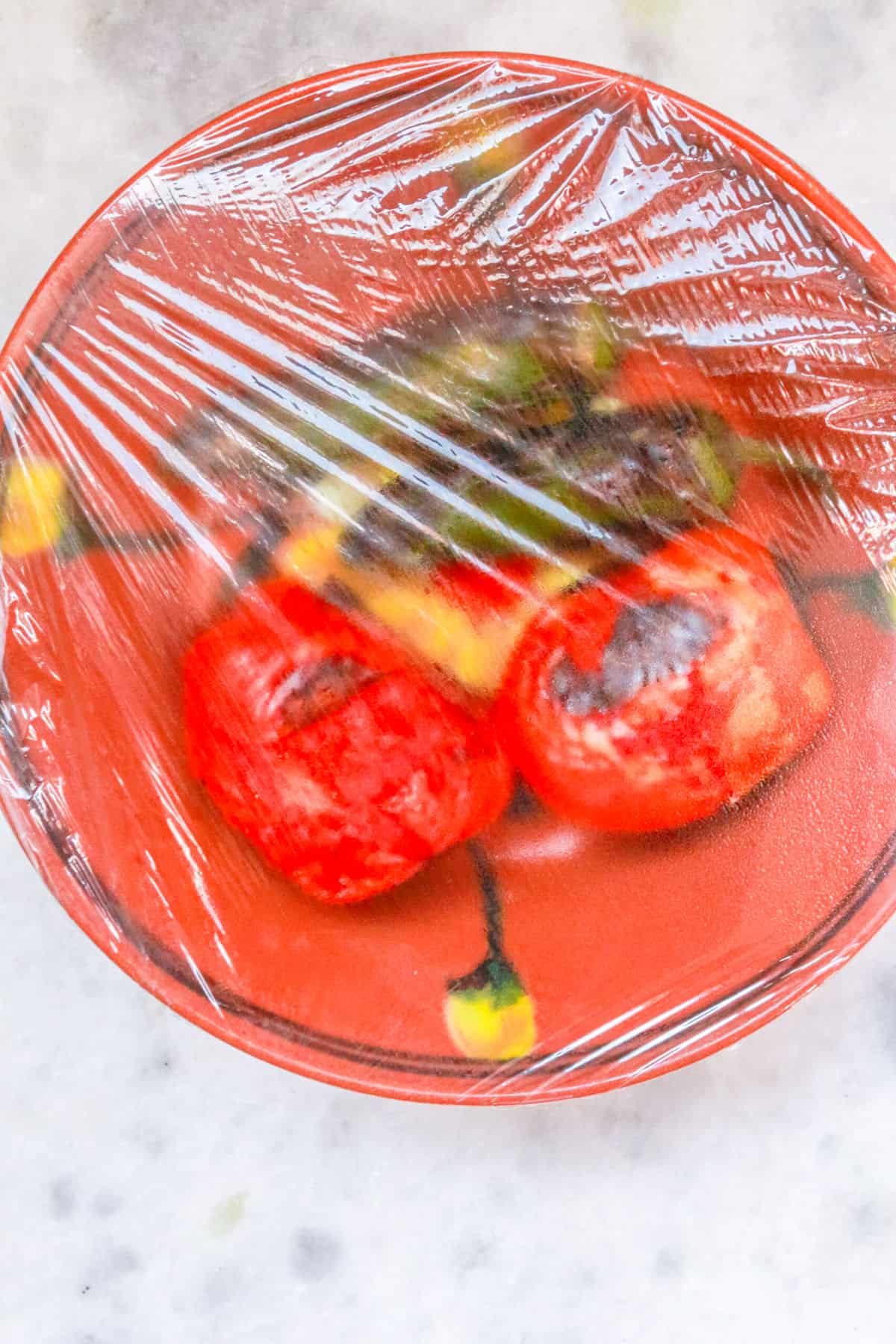 Roasted jalapeños and tomatoes in a bowl covered with plastic-wrap