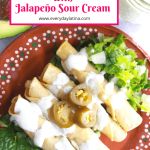 4 flautas on a brown plate over a bed of lettuce and drizzled with jalapeño sour cream