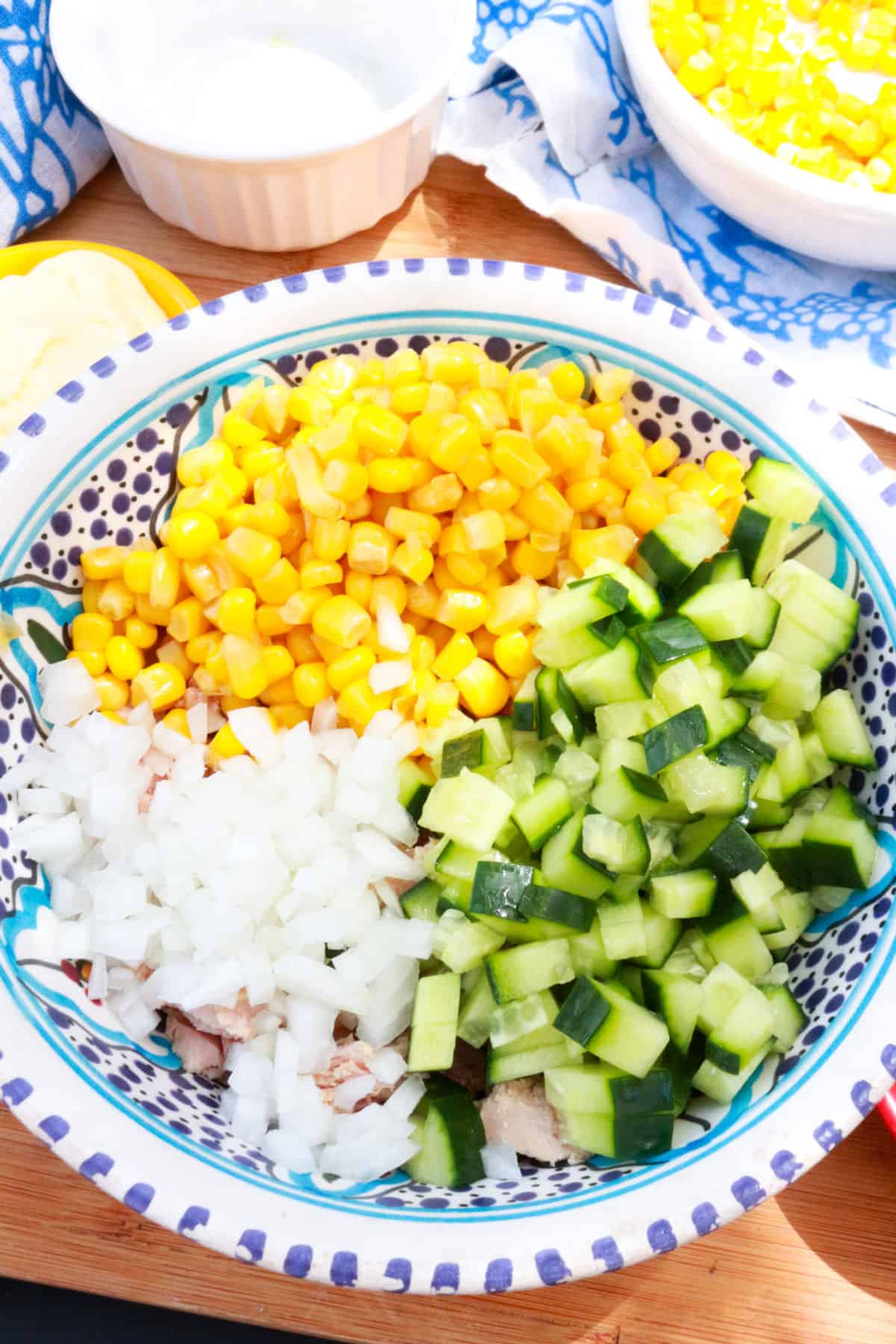 A bowl with canned corn, diced cucumber and diced onion.