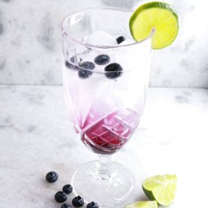 Tall glass with blueberry mocktail garnished with blueberries and lime