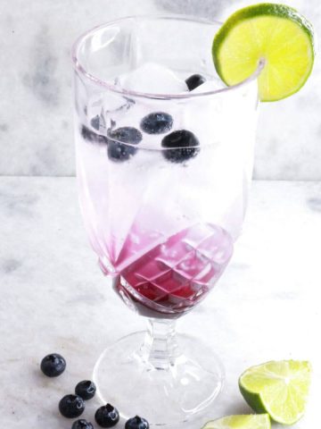 Tall glass with blueberry mocktail garnished with blueberries and lime