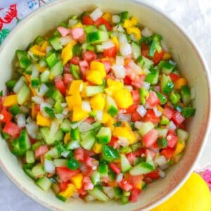 Mango pico de Gallo in a bowl with a mango and wooden spoon by it