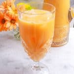 Agua de Melon in a glass with a pitcher and flowers behind it