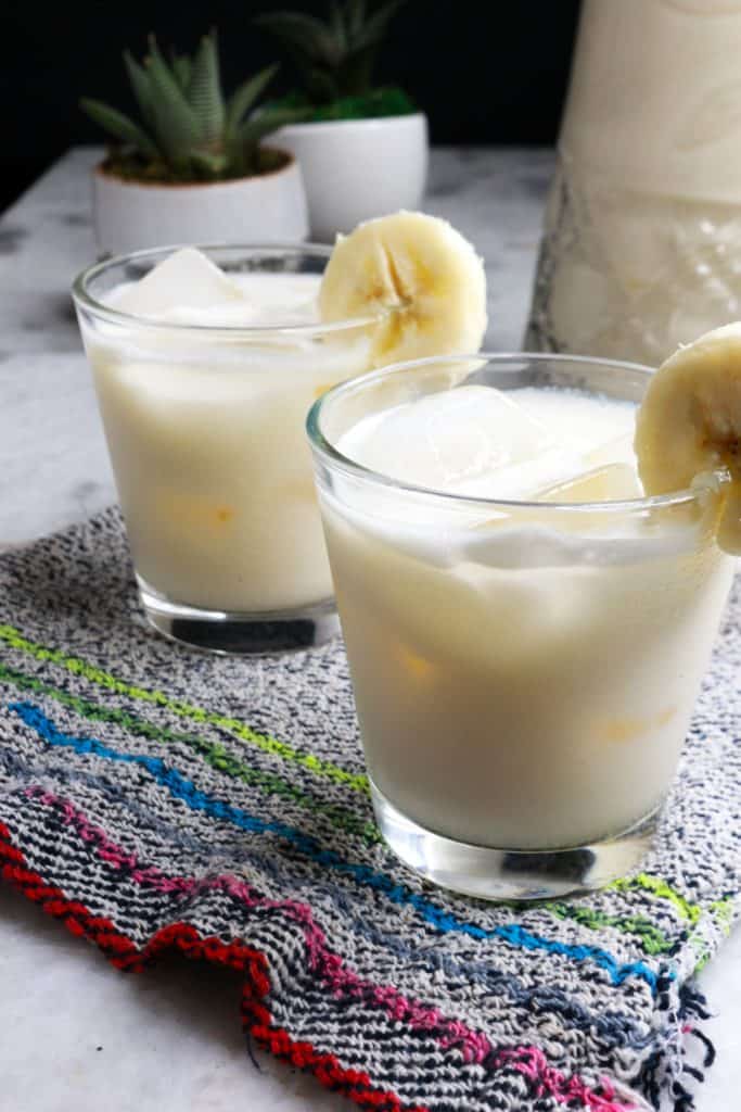 Two glasses with ice and agua de platano garnished with a slice of banana