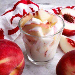 Glass with dairy-free duraznos con crema surrounded by fresh peaches