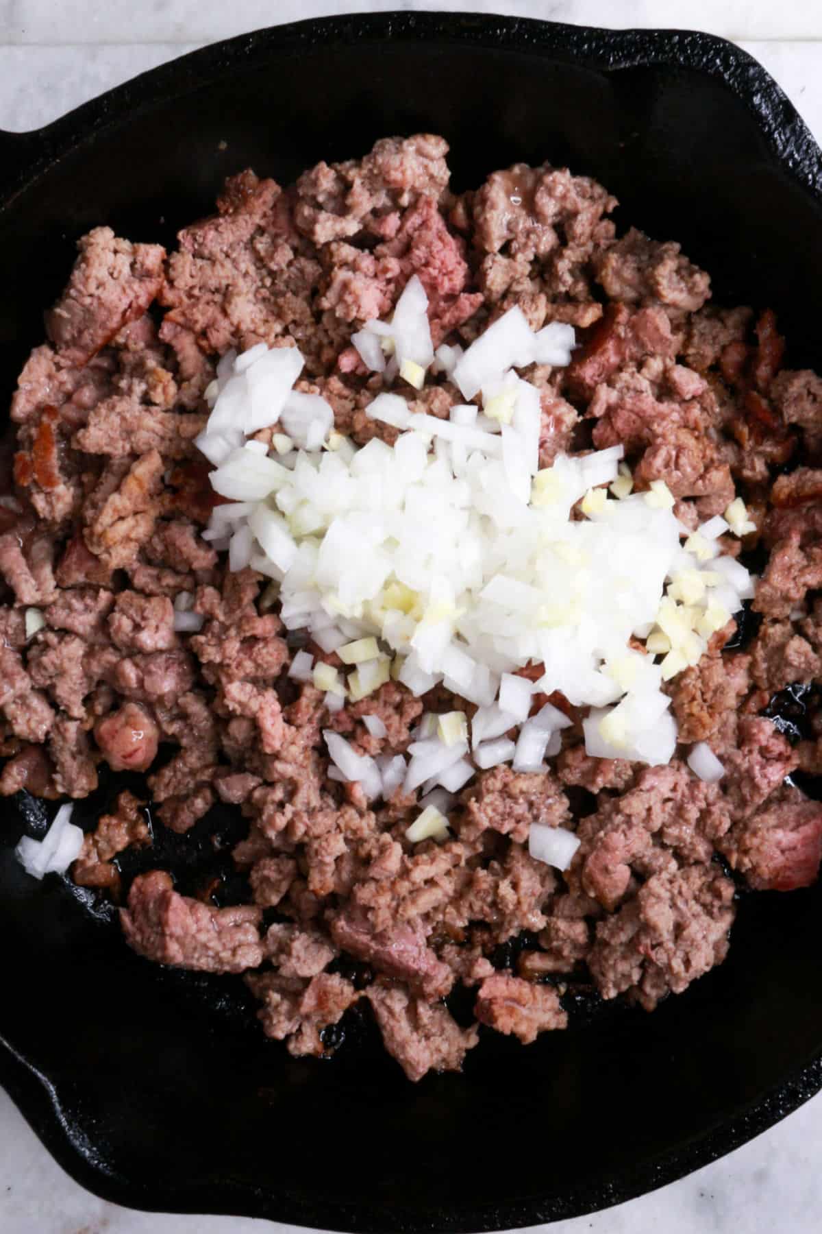 Ground beef in a cast iron with diced onion and garlic