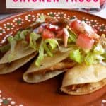 Three crispy chicken tacos on a Mexican plate, topped with garnishes