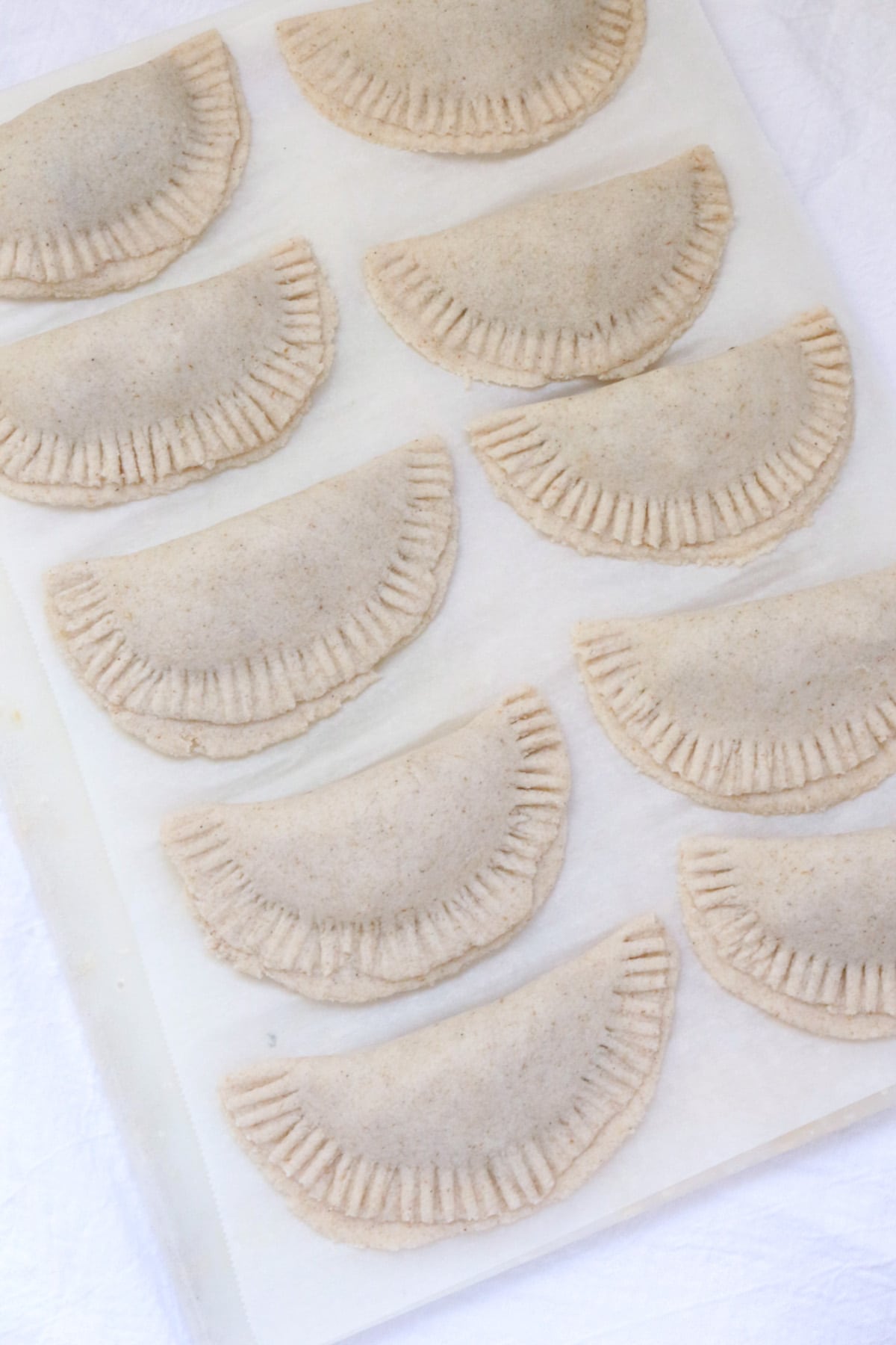 Gluten-free empanadas ready to be fried, sitting on a piece of parchment paper