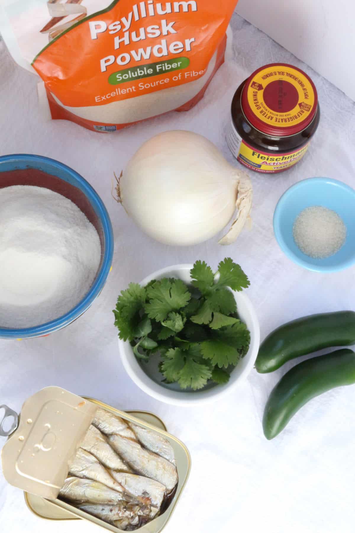 Psyllium husk powder, yeast, an onion, a bowl office flour, cilantro, salt, jalapeños and a can of sardines