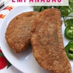 Two gluten-free empanadas de sardina on a plate with cilantro and jalapeño slices beside them.