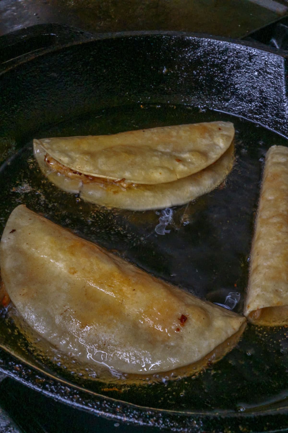 Three chicken tacos being fried in a cast-iron skillet