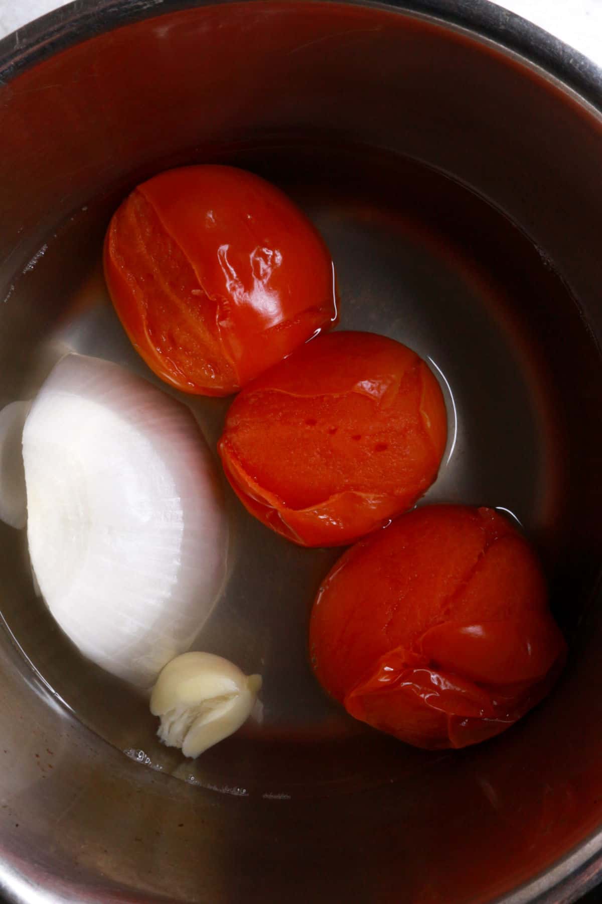3 tomatoes, a piece of onion, garlic and water in a small pot