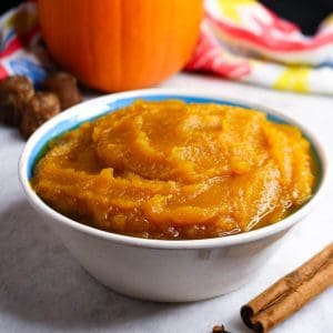 A close up of a bowl of puré de calabaza with a pumpkin and some piloncillos in the background
