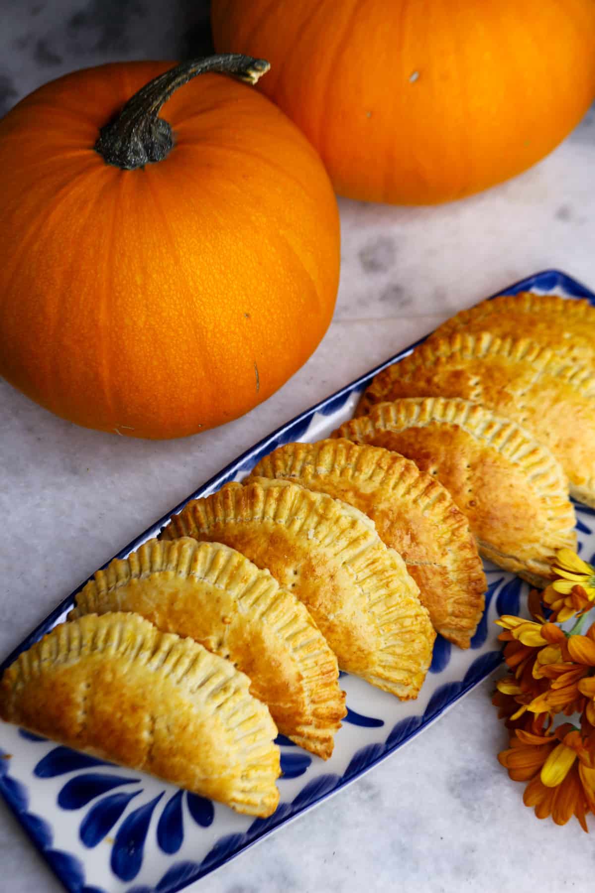 Gluten-free empanadas de calabaza on a long plate with two pumpkins behind them.