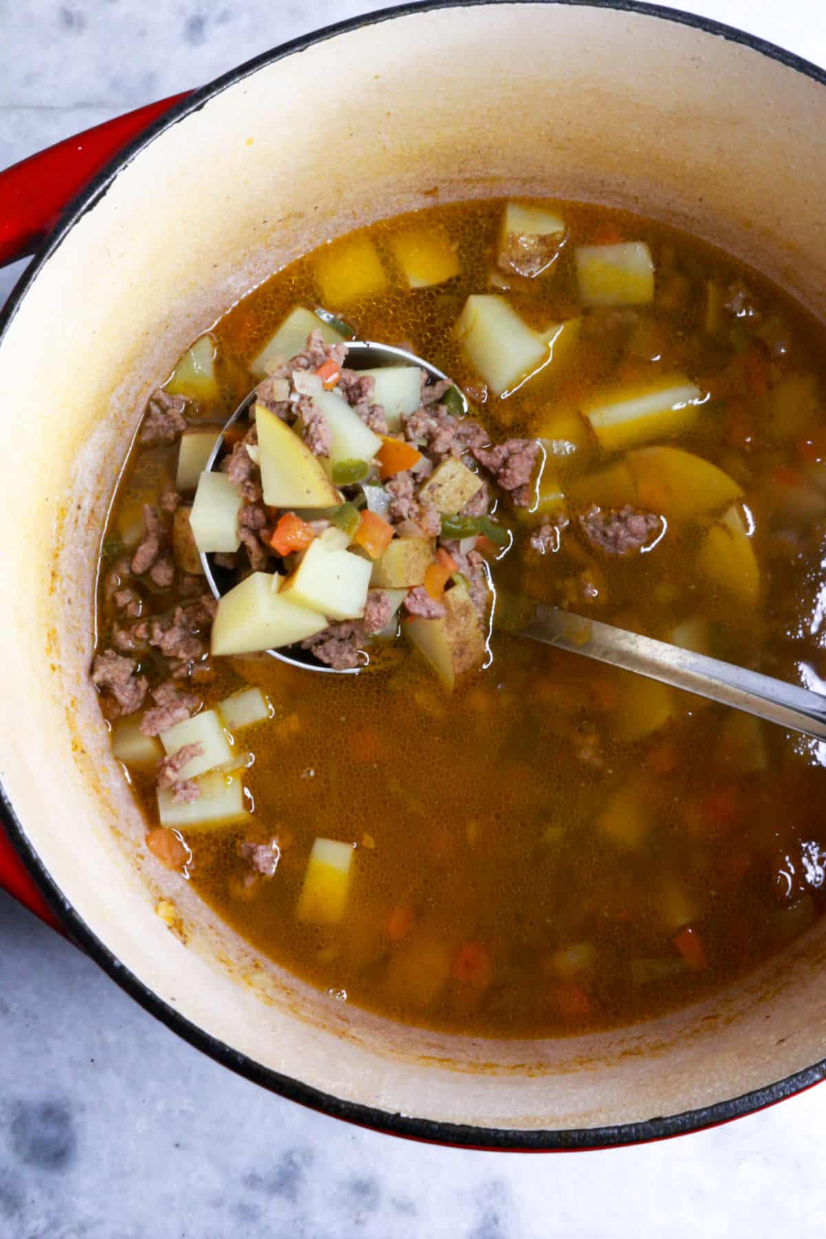 A ladle scooping ground beef stew with jalapeño