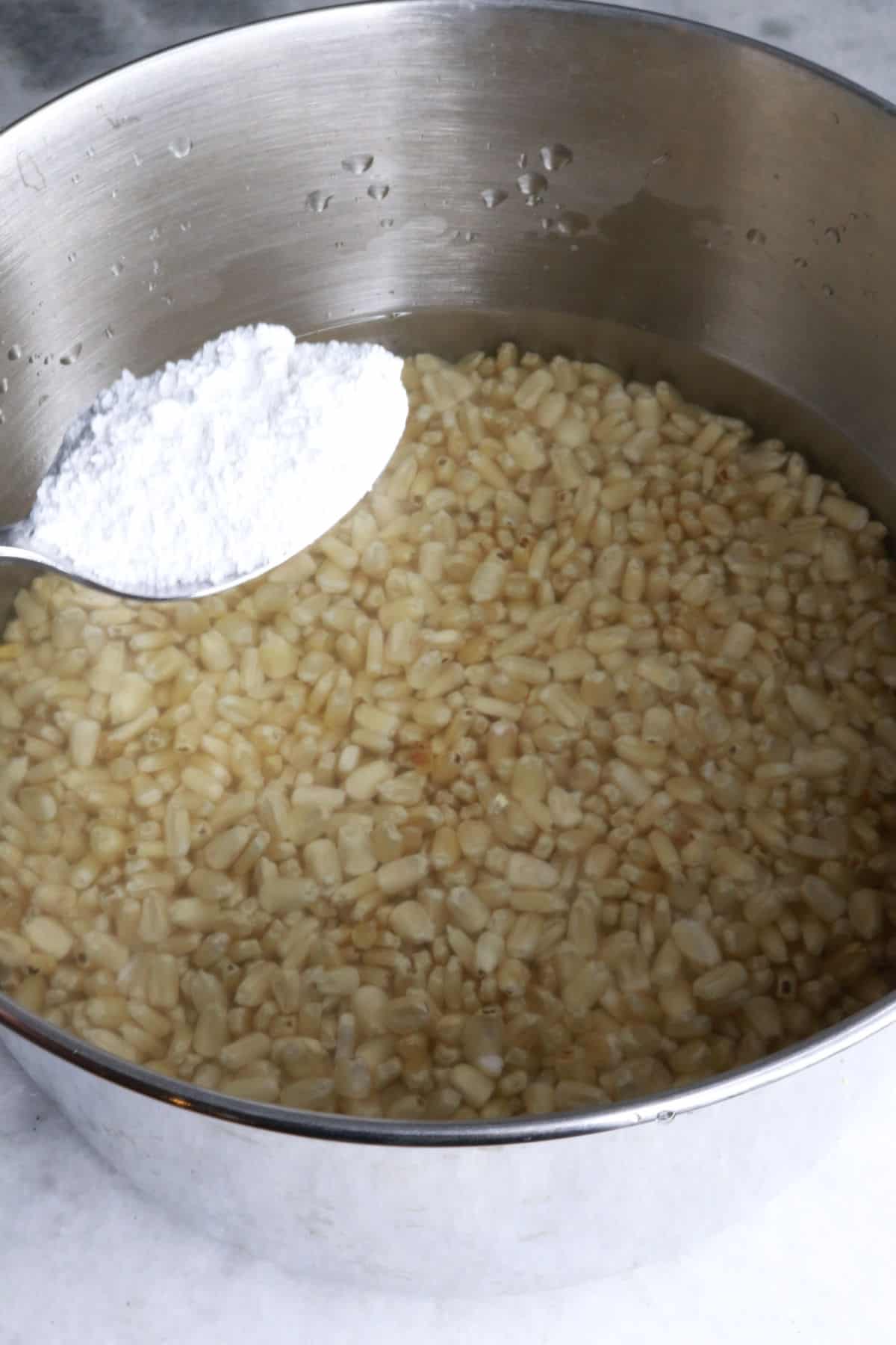 Adding a spoonful of cal to a pot of water and corn 