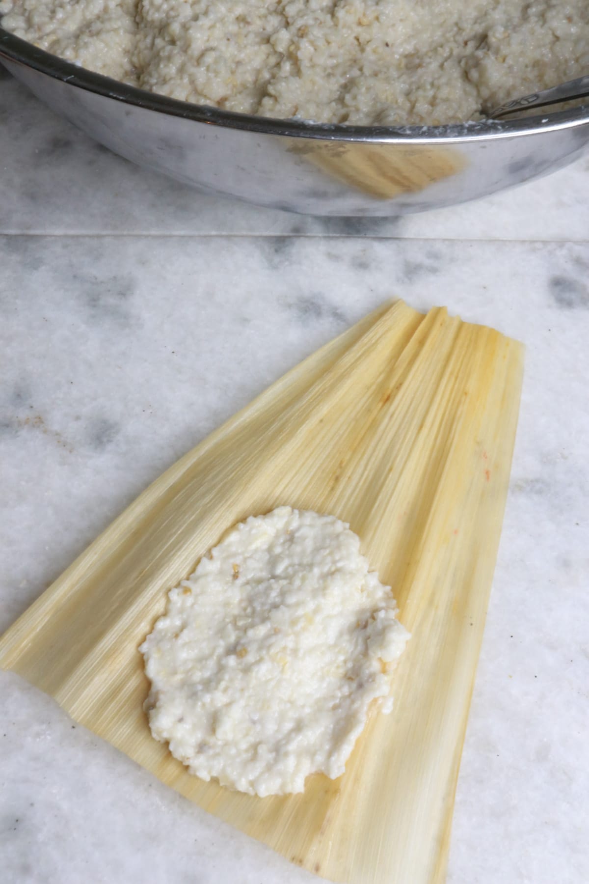 A corn husk with masa for tamales spread on it and a big bowl with masa