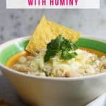 Side view of a bowl of white chicken chili with hominy garnished with cilantro and a few tortilla chips