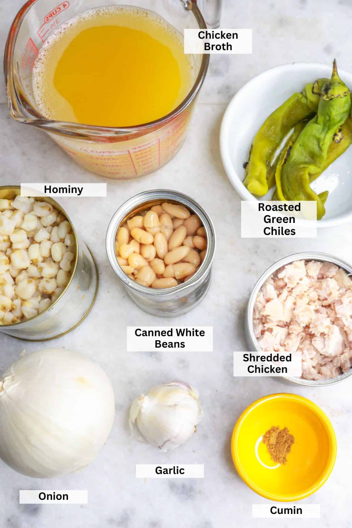 Ingredients for white chicken chili with hominy: broth, green chiles, hominy, white beans, chicken, garlic, onion, cumin
