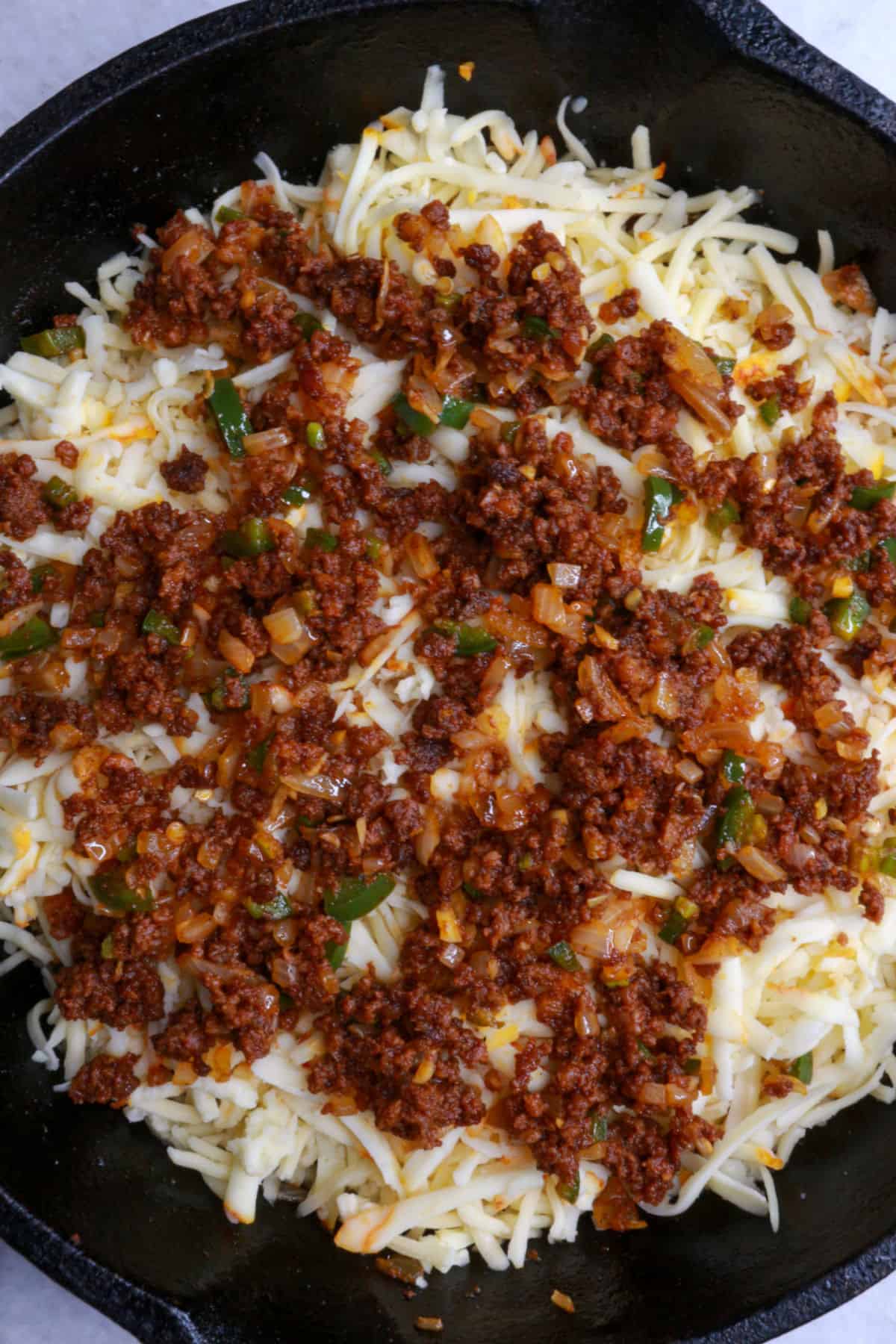 Shredded cheese topped with chorizo in a cast-iron skillet