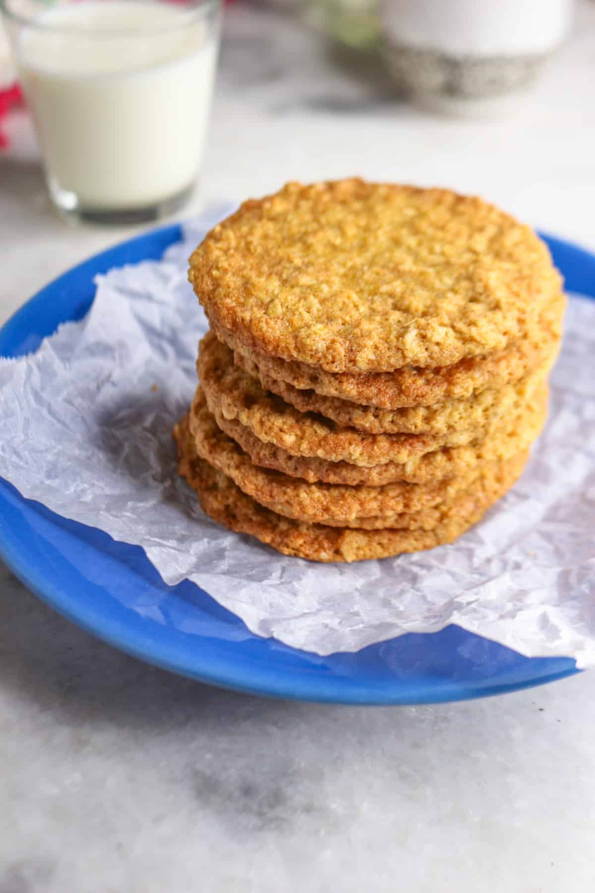 Coconut flour oatmeal cookies stacked on a blue plate with a glass of milk behind it.