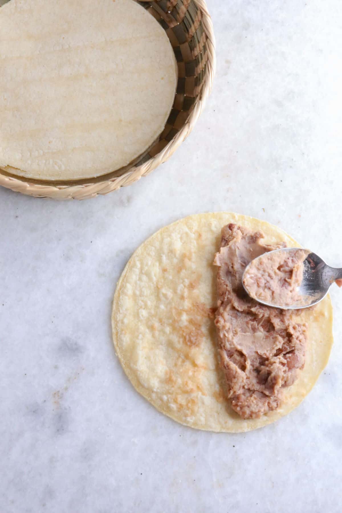 Using a spoon to spread refried beans on a warm corn tortilla