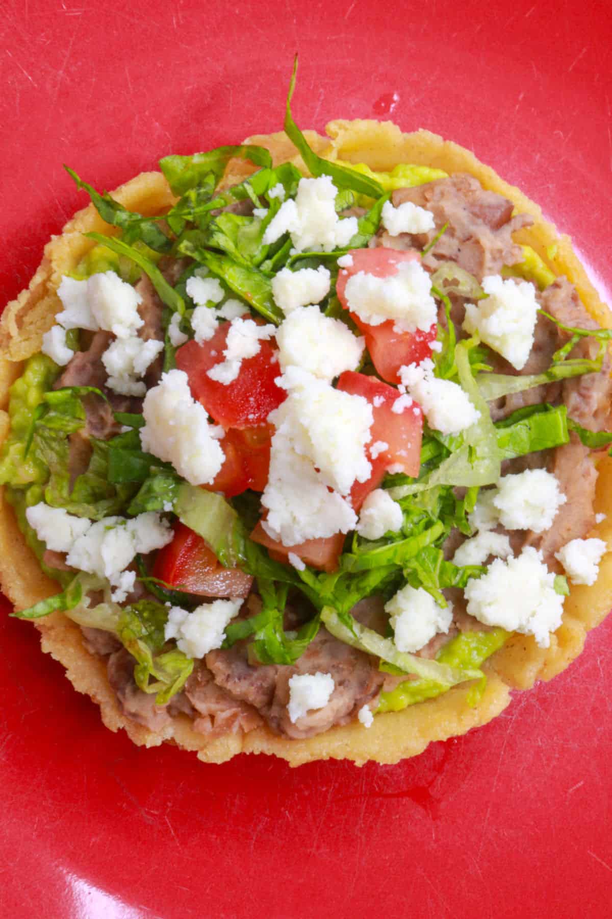 Sope de frijoles garnished with lettuce, tomato and queso fresco