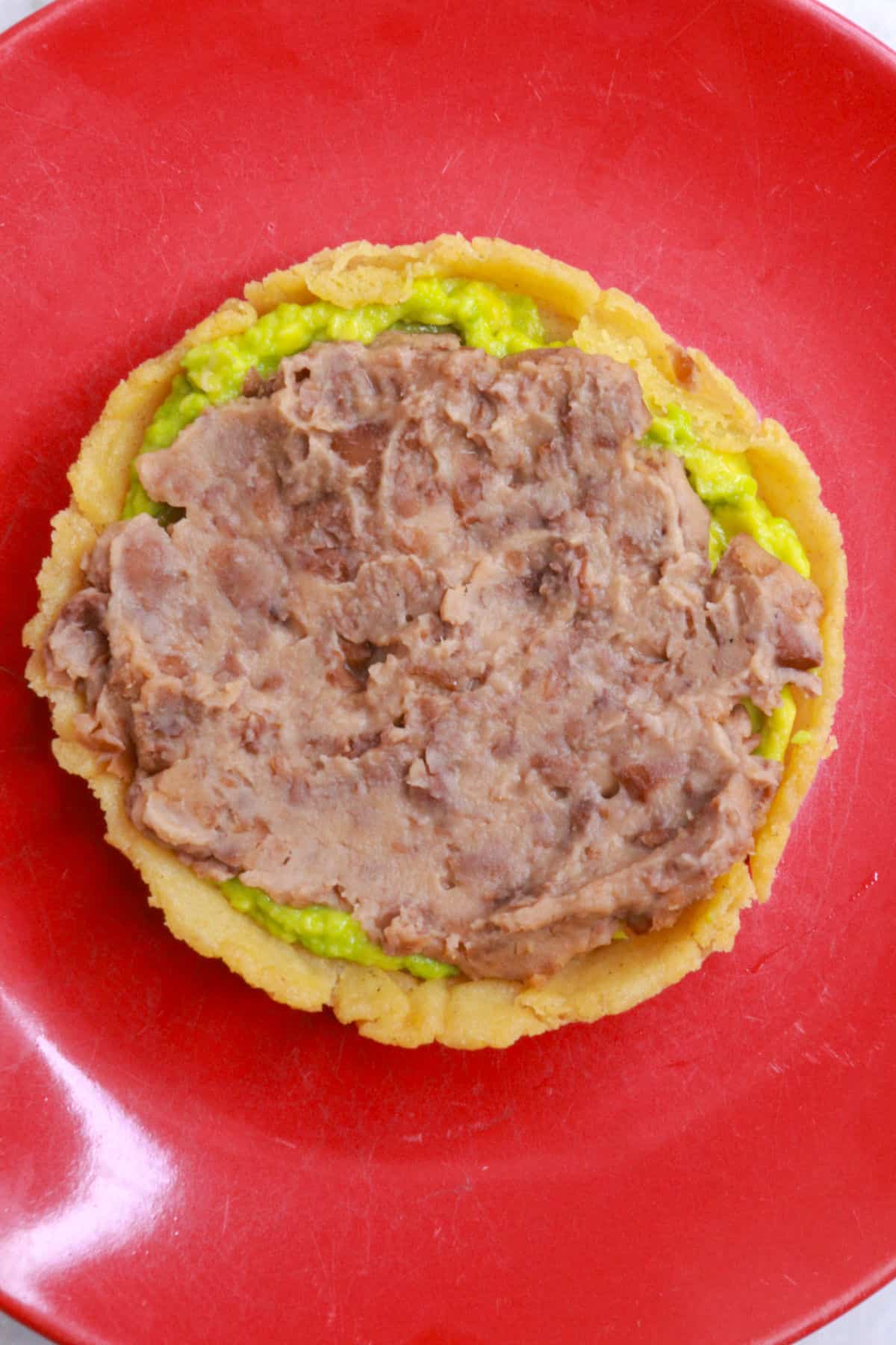 A sope topped with mashed avocado and refried beans