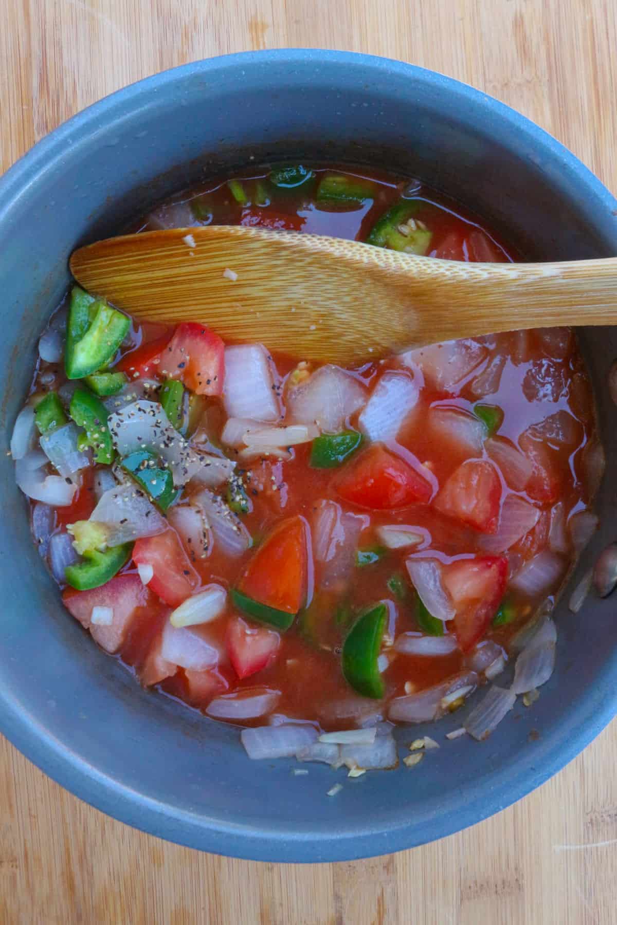 A wooden spoon mixing a chunky jalapeño salsa in a small pot
