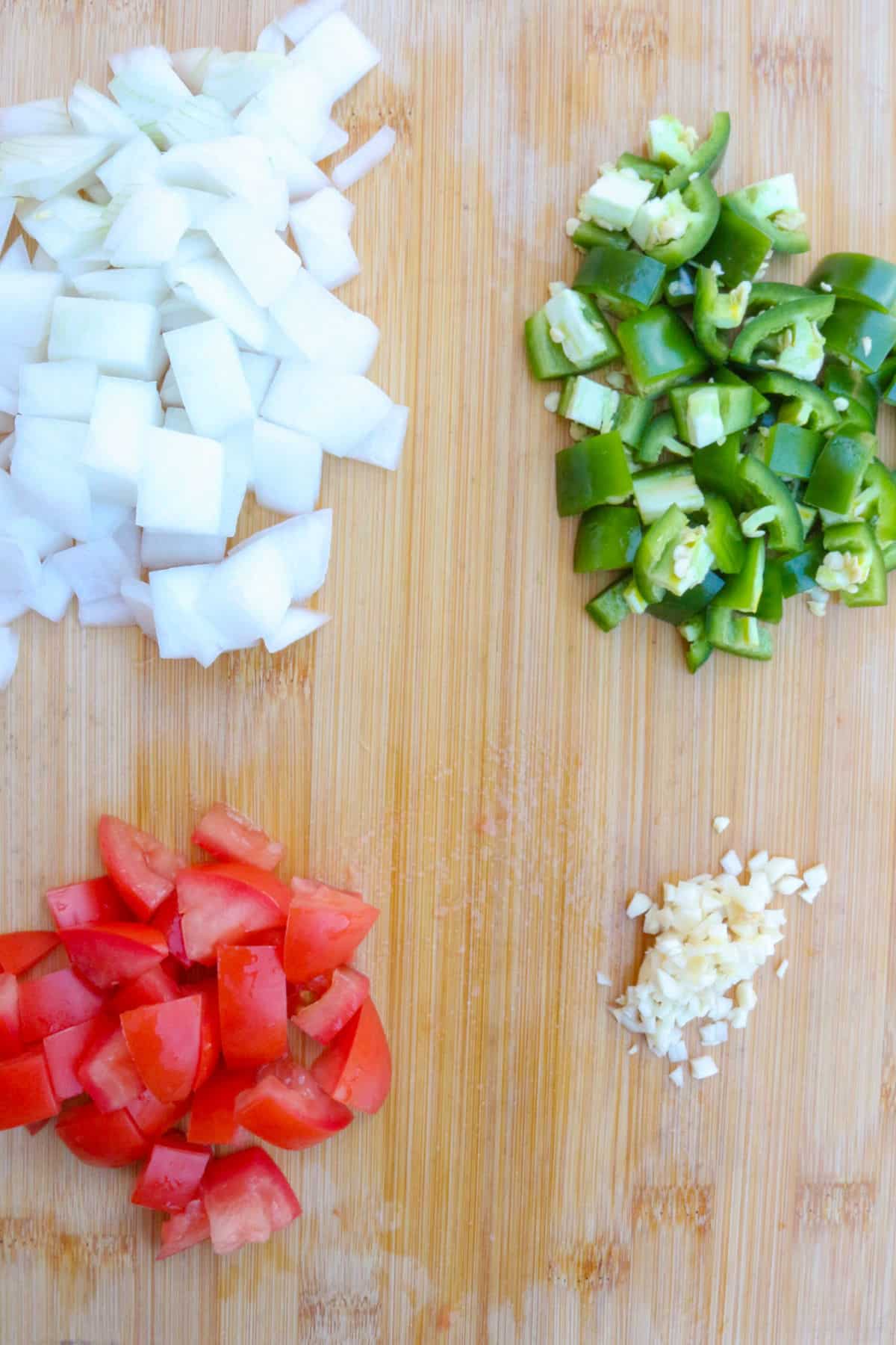 Chopped onions, jalapeños, tomatoes and garlic on a wooden cutting board