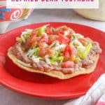 A red plate with a tostada de frijoles (refried bean tostada)
