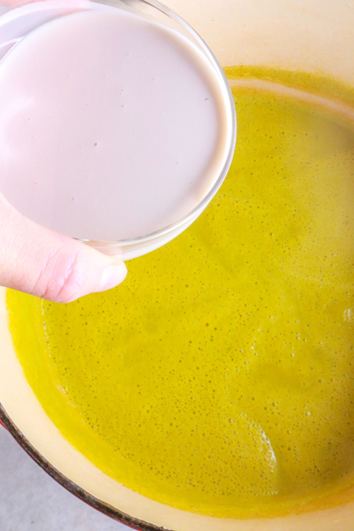 Adding cream to a pot of asparagus soup