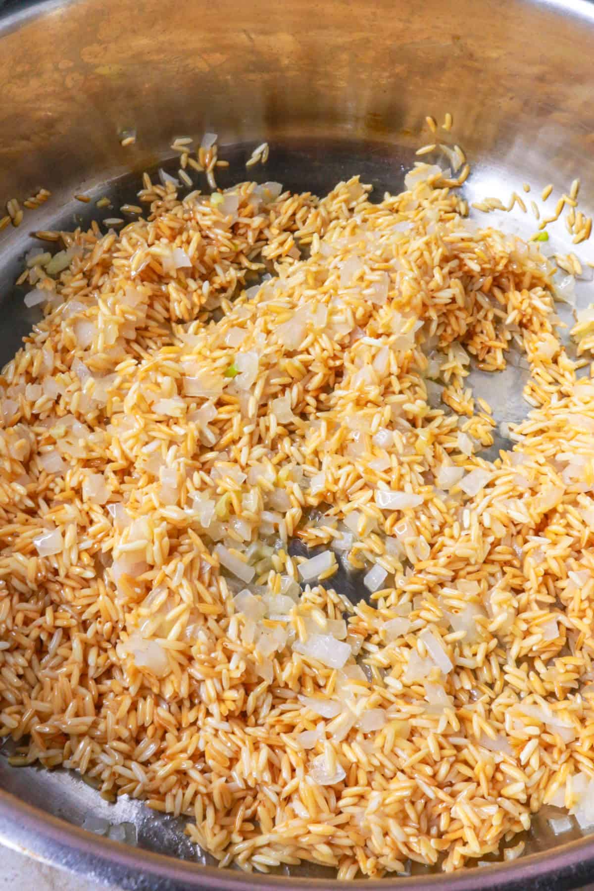 Toasted rice mixed with diced onion and garlic in a pan
