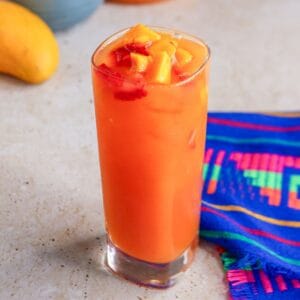 Glass of strawberry mango Agua Fresca garnished with pieces of fruit