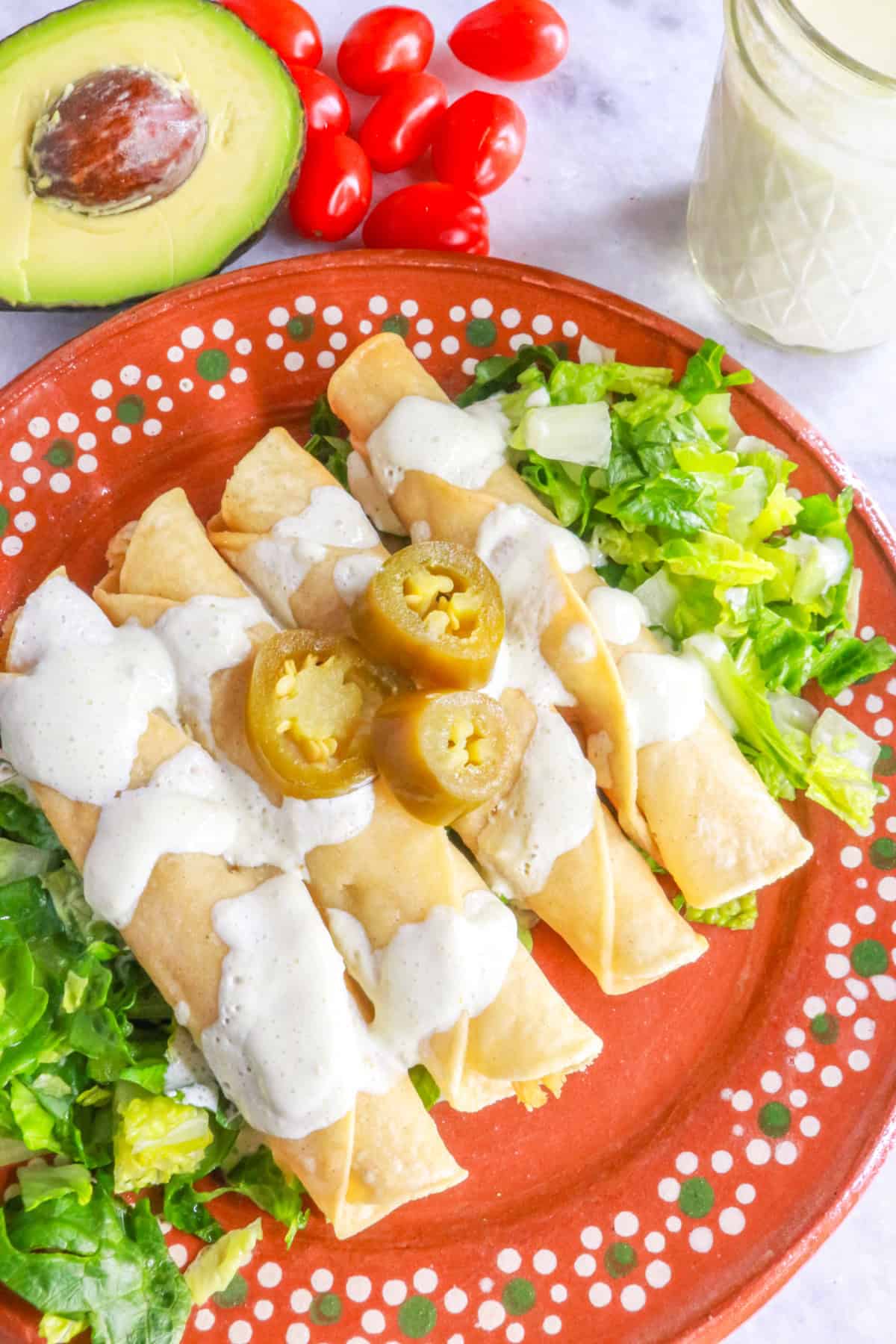 Flautas de pollo garnished with jalapeño sour cream on a Mexican plate