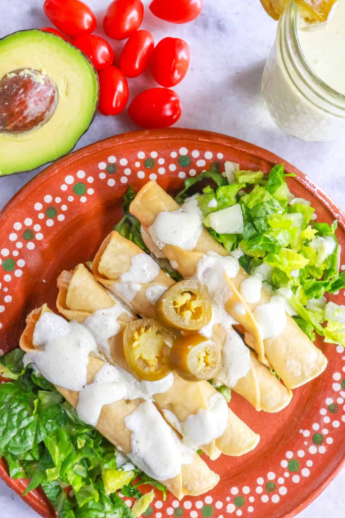 Flautas de pollo garnished with jalapeño sour cream on a Mexican plate